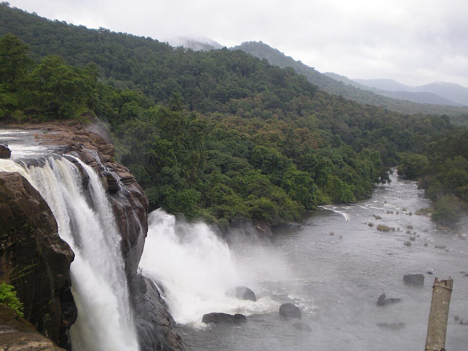Athirappilly waterfall dropping into the river beside forested hills